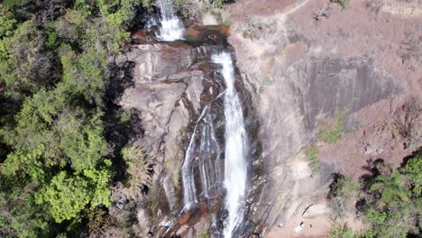 Aerial-view-of-a-waterfall-falling-down-from-a-steep-mountain-surrounded-by-forests