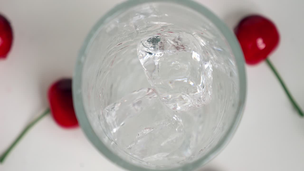 새 눈 가까이 찍은  ⁇ 은 얼음 큐브가 차가운 음료를 위해 유리잔에 떨어지는 동안 체리는 느린 움직임으로  ⁇ 에 누워 있습니다