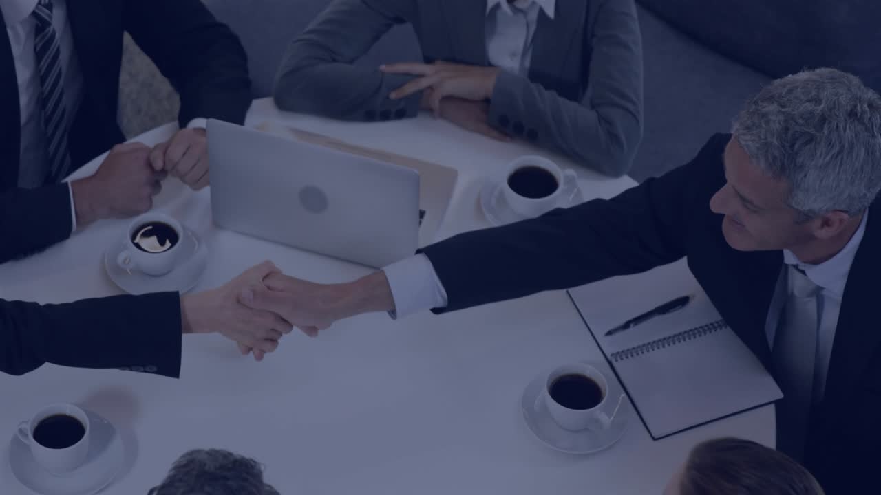 Two business colleagues clasping hands over table, sparking HUD icons pulsing into grid over laptop
