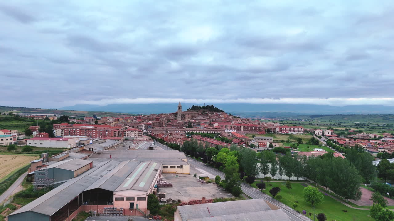 Forward aerial view of Navarrete village, La Rioja, Spain. Scenic townscape with church, rooftops, vineyards and hills under cloudy sky
