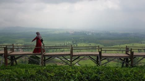 young woman wearing muslim dress walking on wooden bridge with beautiful view of nature in the tea plantations