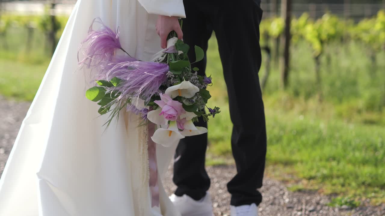 Bruden holder en buket, mens brudgommen krammer i vinmarken, kameraet vipper op, filmisk