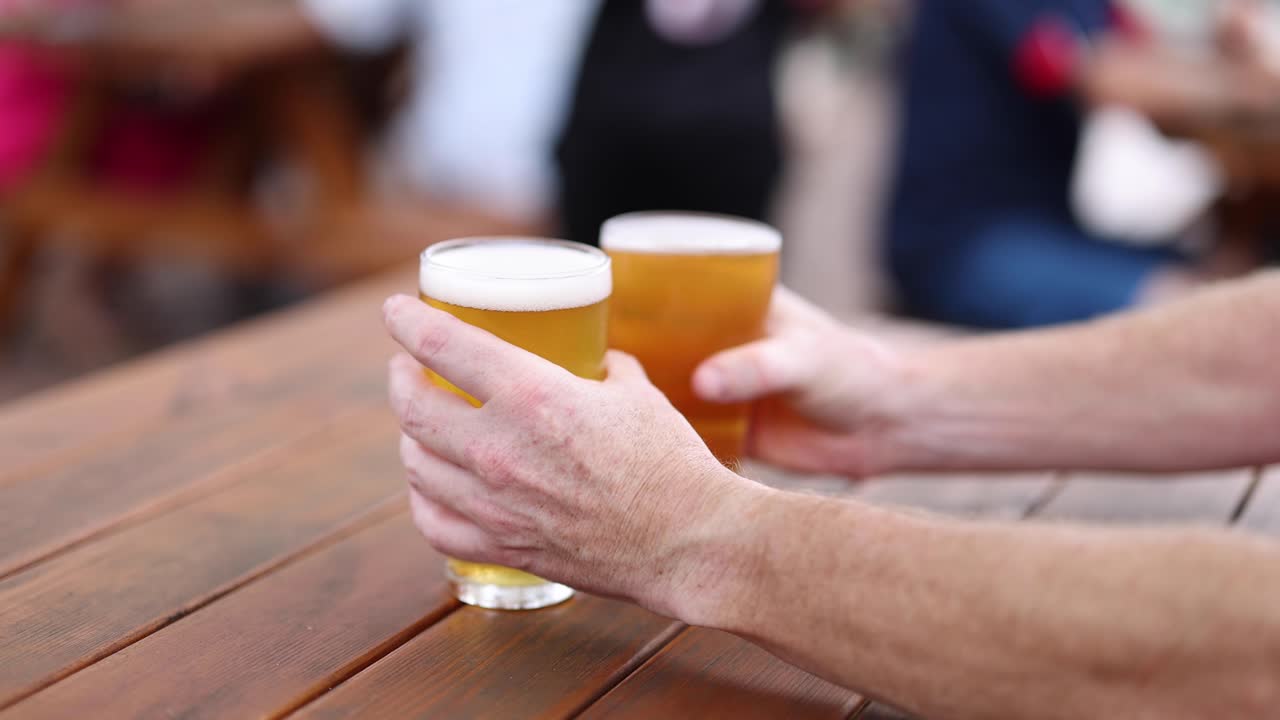 Açık havada bira kadehleri tokuşturan iki kişi.