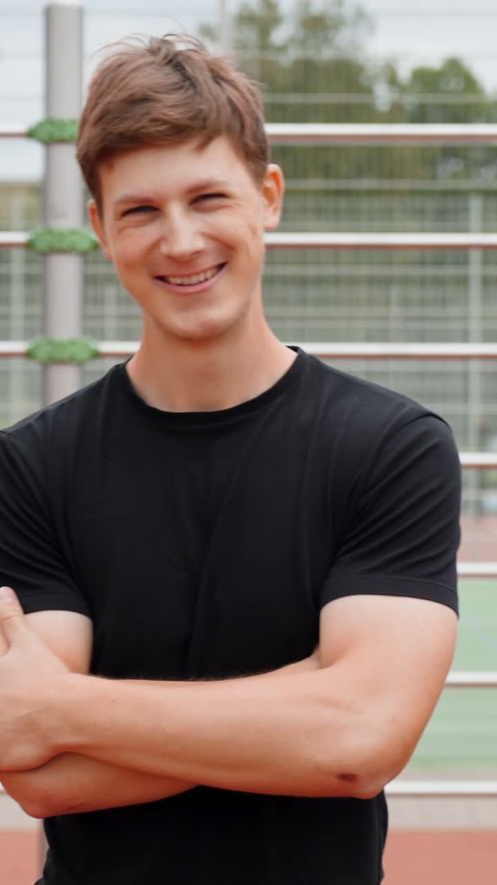 Vertical shot of athletic young man smiling outdoors on sports court