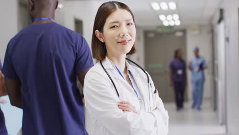 video portrait of smiling asian female doctor standing in busy hospital corridor, copy space