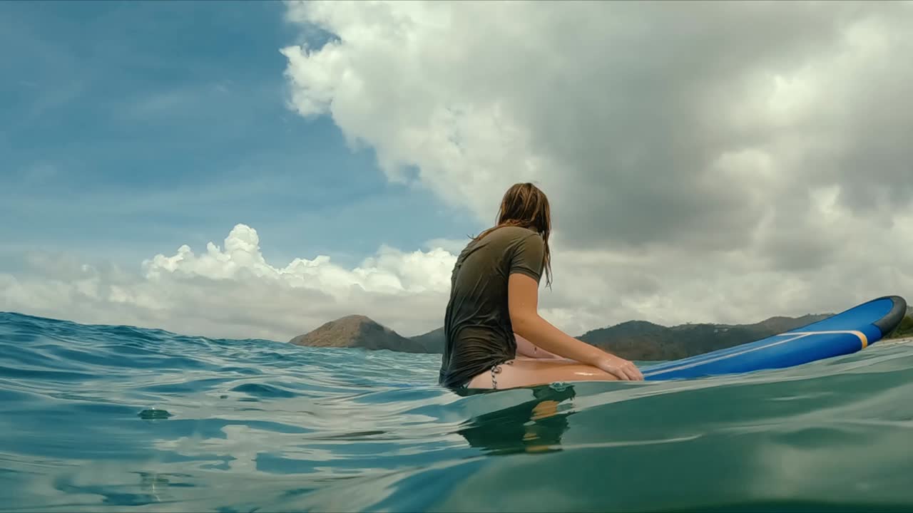 mujer surfista sentada en una tabla de surf esperando una gran ola