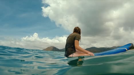 female surfer sitting on surfboard waiting for a big wave