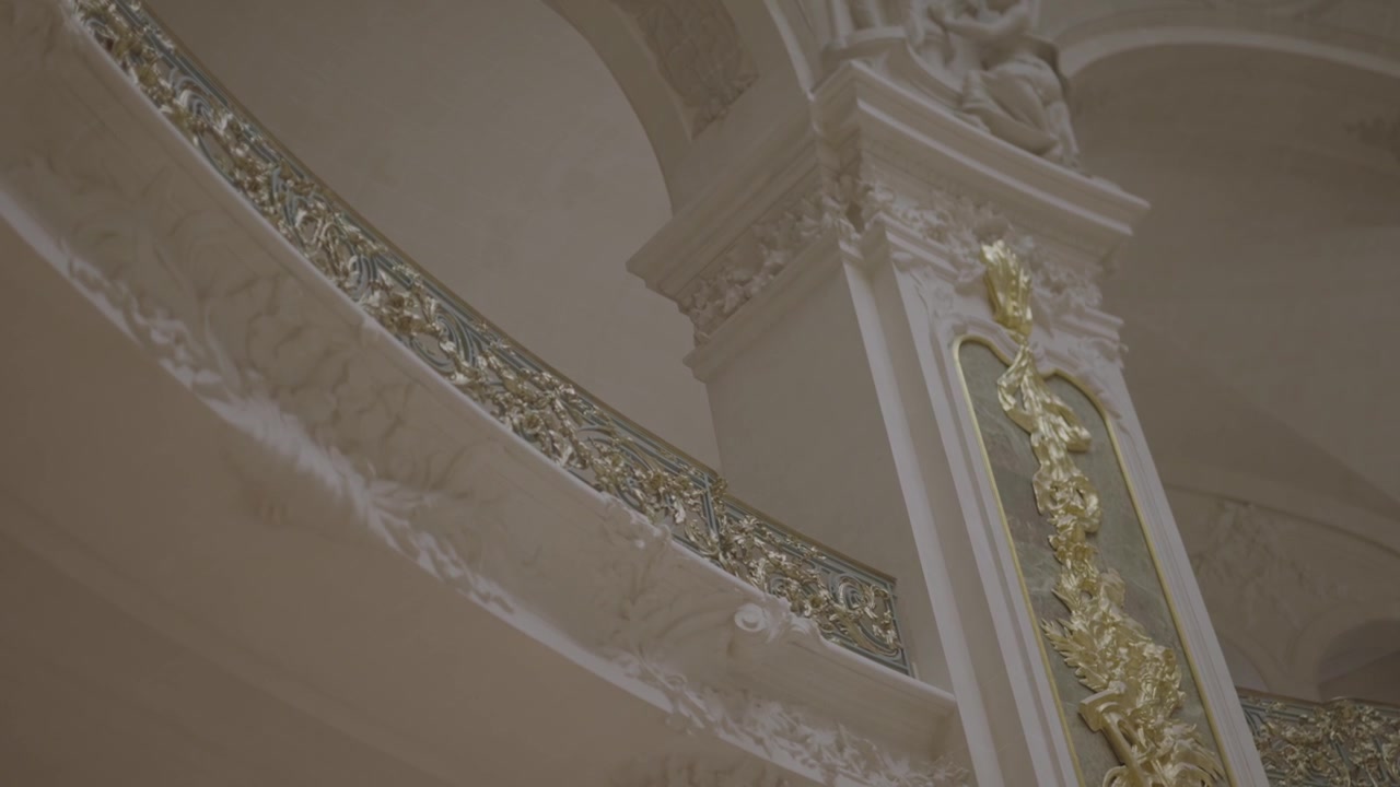 Vista aproximada de um elegante corrimão dourado de escada em espiral dentro de um grande edifício parisiense, exibindo detalhes finos em ouro contra pedra branca.