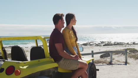 happy caucasian couple sitting in beach buggy by the sea talking