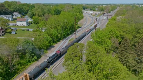 a steam engine moving freight cars in yard along the tracks surrounded by vibrant greenery in a tranquil rural setting.