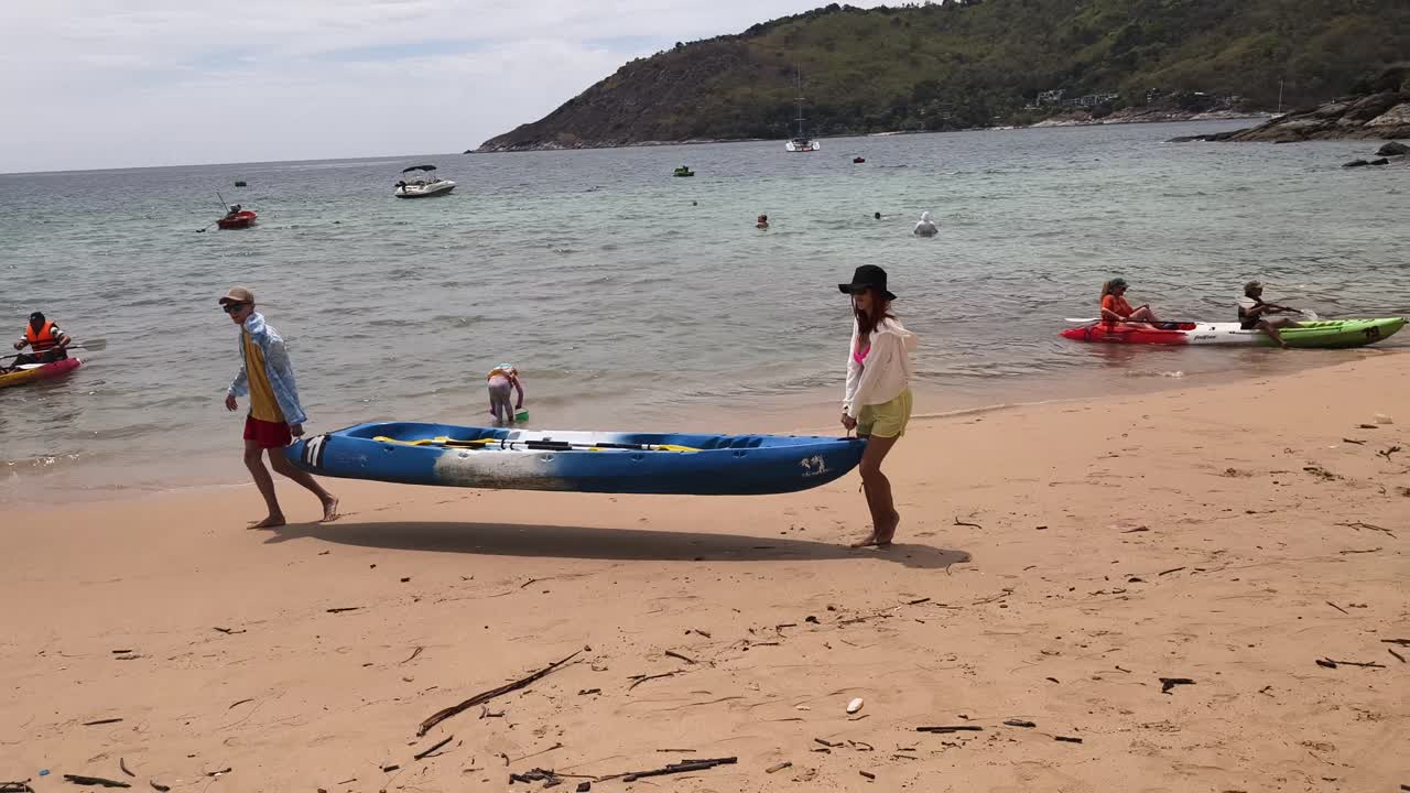 People carrying a kayak on a tropical beach