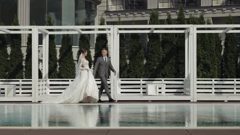 Newlyweds-caucasian-bride-groom-walking-near-swimming-pool,-holding-hands,-wedding-couple-family