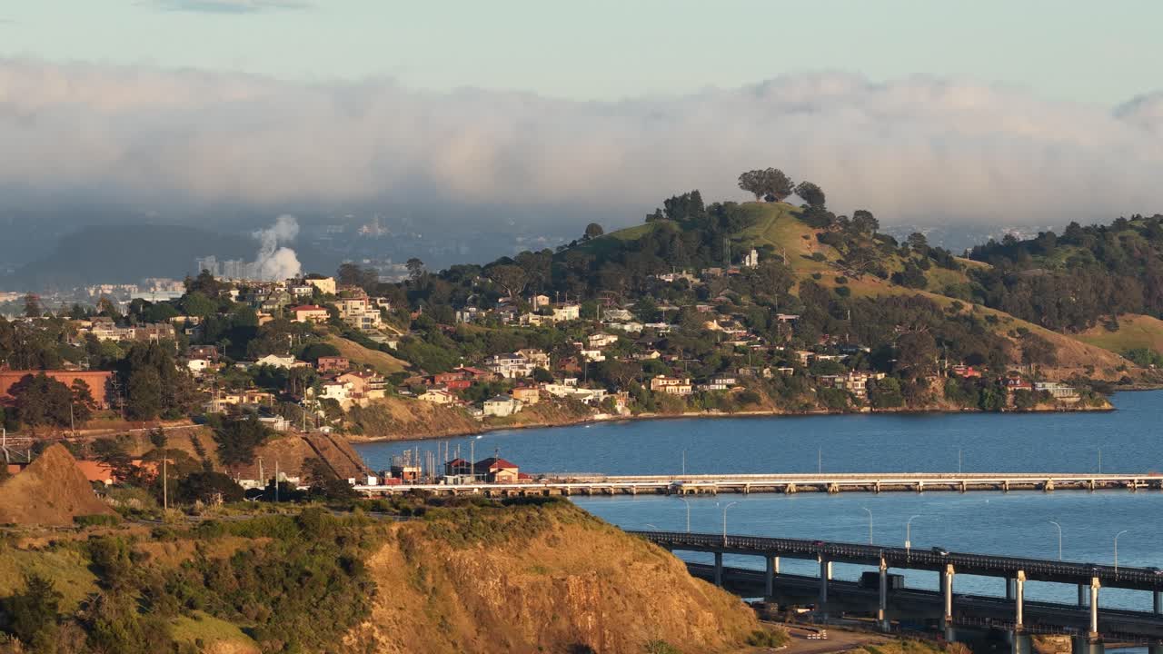 Ripresa aerea con drone in movimento che mostra il ponte Richmond San Rafael che attraversa la baia di San Francisco, con auto che lo percorrono e la costa collinare coperta dalla nebbia mattutina