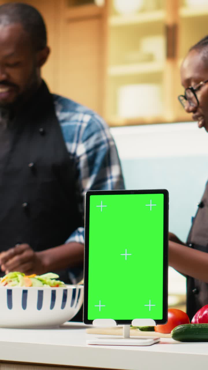 Vertical Video Vertical green screen on tablet next to black people preparing food in the kitchen