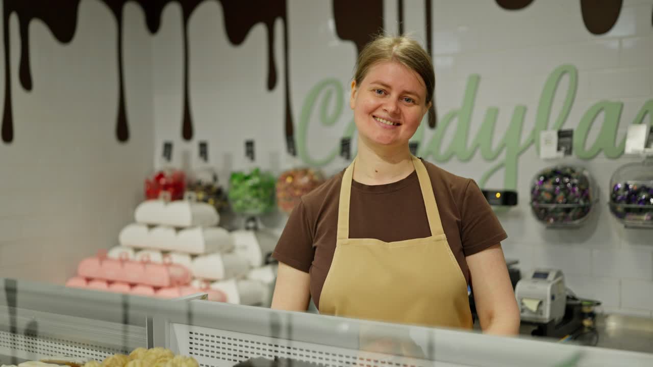 Portrait of a happy girl in a brown T-shirt who stands behind the counter in the confectionery department in a supermarket