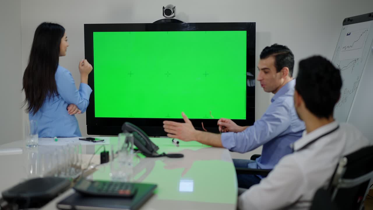 현대적인 사무실에서 크로마키 모니터와 사려 깊은 다민족 동료가 브레인 스토밍을 하고, 프로 밀레니얼 동료 그룹이 녹색 화면을 보고 실내에서 프로젝트를 논의합니다.