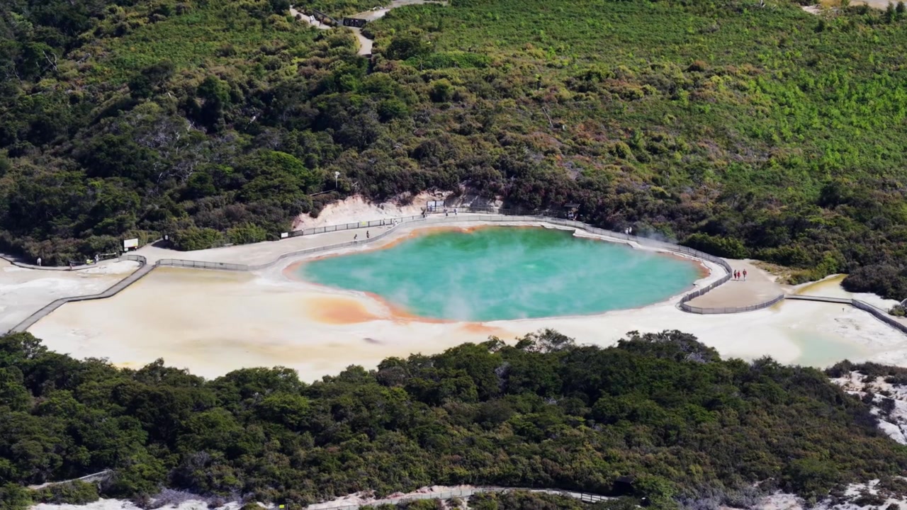 Geotermální bazén Wai-O-Tapu poblíž Rotorua, Nový Zéland, tyrkysová termální voda, barevné minerální usazeniny, turistické stezky a původní vegetace z výšky.