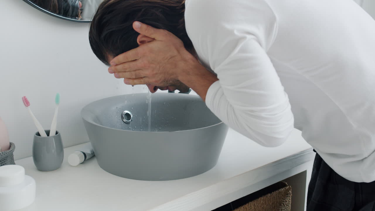 человек моет лицо в ванной.