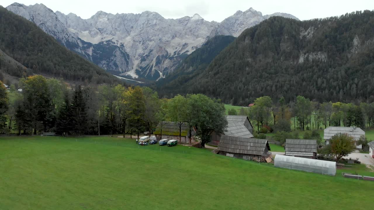 Drone flying away from campervans as it shows more of the mountains and farms in the background. Jezesko Valley in Slovenia in Autumn season aerial view