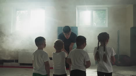 kids group listens to sensei at martial arts class. little fighting students wave hands in front of instructor to prepare exercising in gym slow motion