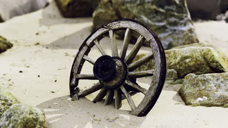 old wooden wheel partially buried in sandy beach surrounded by rocks