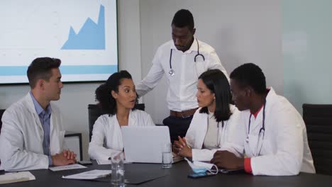 Diverse-group-of-doctors-in-discussion-in-meeting-room-using-laptop