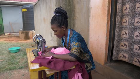 side view of an african lady sewing clothes on a manual tailoring machine outside her small house