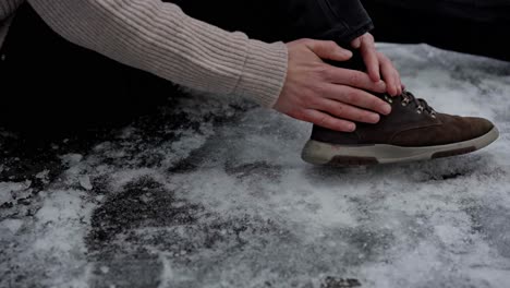 man sitting on ice grabs injured ankle, examines cut on hand after slipping