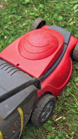close-up work of electric lawn mower. red and black cutting machine trimming grass in the backyard. vertical video