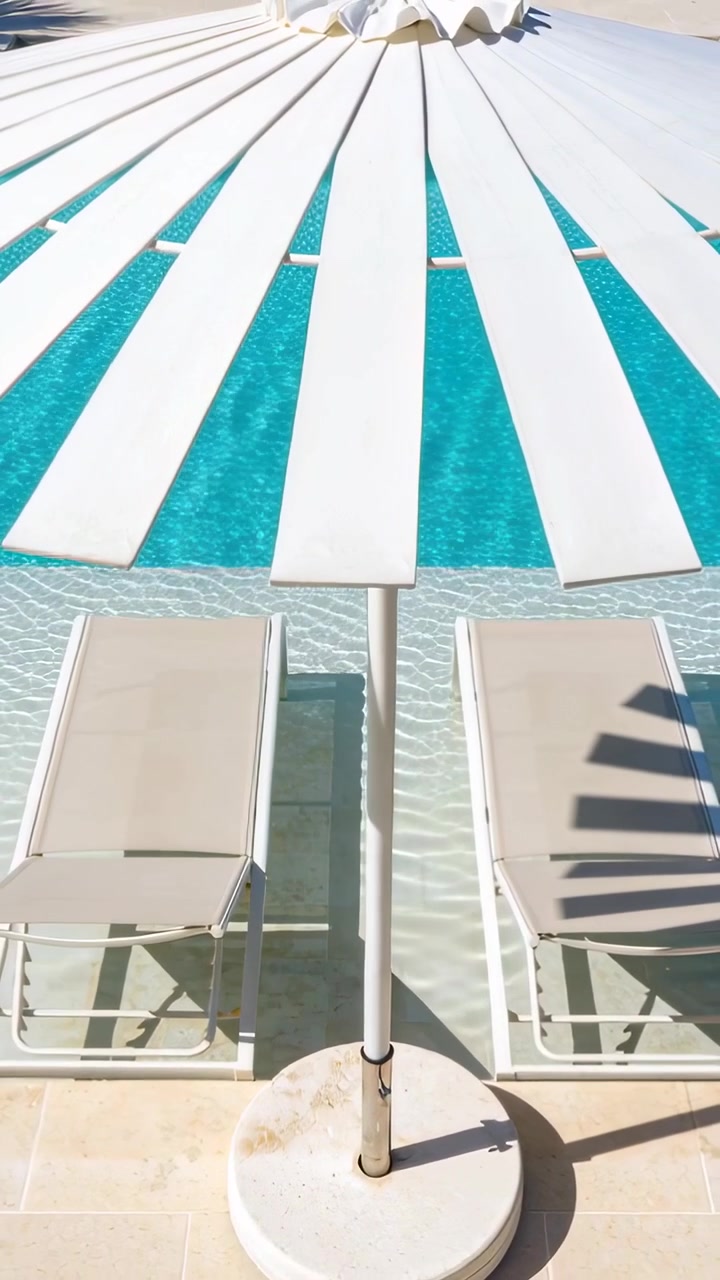 Vertical video: Shifting camera revealing white umbrella by pool, palm shadow moving over ripples