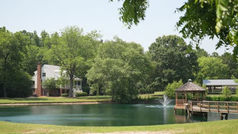 Captura-La-Serena-Belleza-De-Un-Pintoresco-Lago-Con-Un-Encantador-Pabellón-Blanco-En-Medio-Del-Agua,-Con-Una-Prístina-Casa-Blanca-Ubicada-A-Lo-Largo-De-La-Orilla-Del-Lago