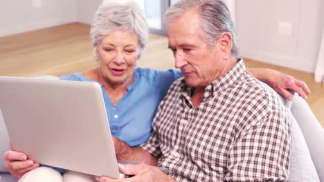 una linda pareja madura usando una computadora portátil en el sofá