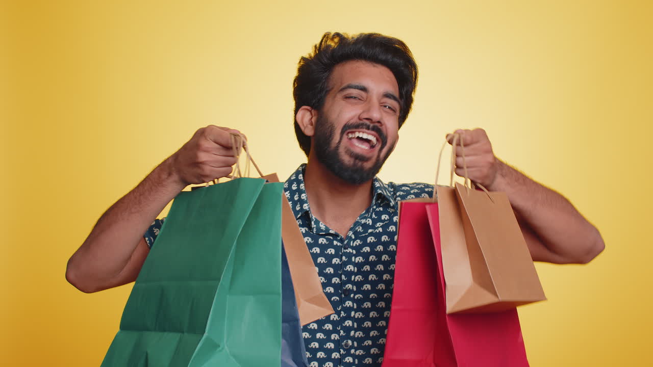 hombre indio mostrando bolsas de compras, descuentos publicitarios asombrado por los bajos precios vacaciones de viernes negro
