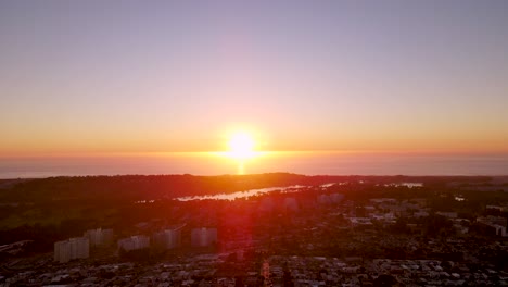 sunset over the ocean and residential houses in foreground drone pan right across the horizon