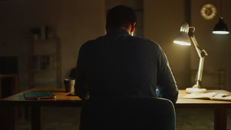 professional creative man sitting at his desk in office studio working on a laptop in the evening. man working with data and analyzing statistics. 360 degree tracking arc shot movement