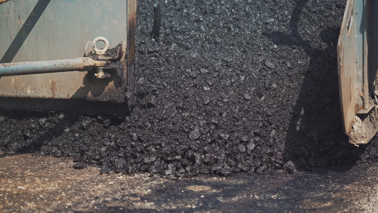 Truck machine for paving apply asphalt to the road. Spillage of asphalt on the street. Pouring blacktopping in a sunny day. Road work, street repair. Close-up. Slow motion.