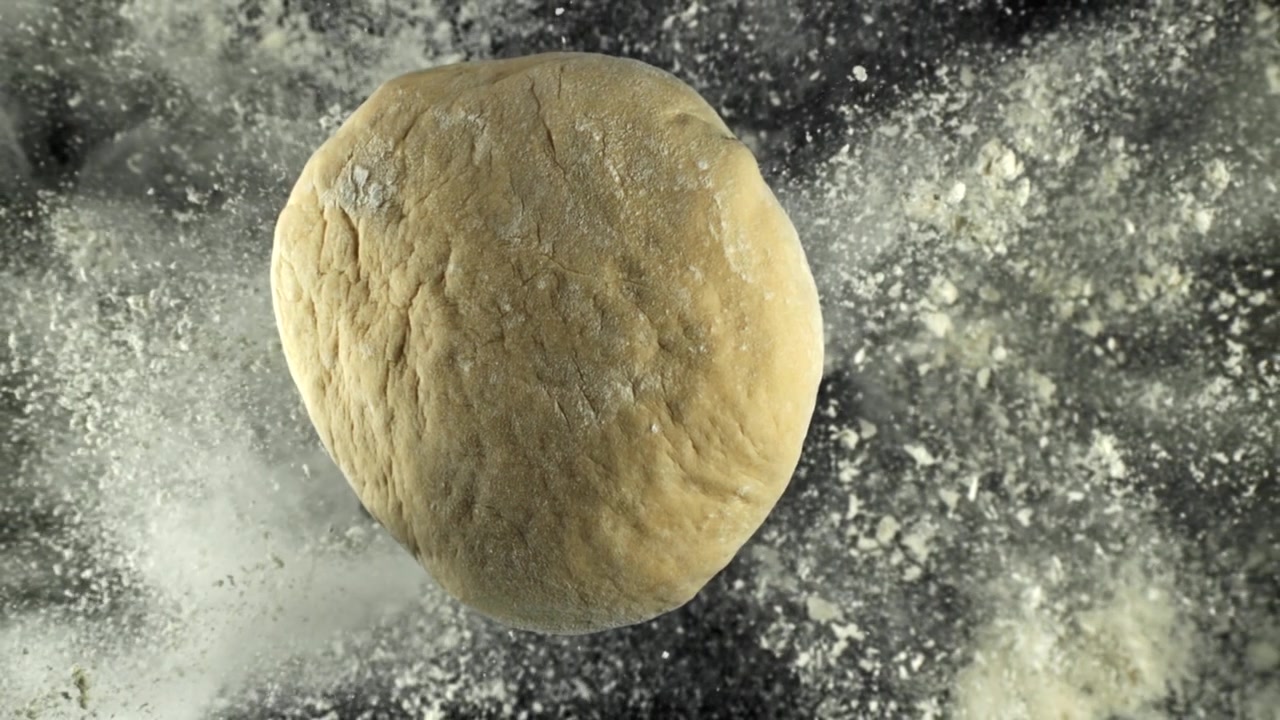 Fresh Dough Ball Surrounded by Falling Flour on a Dark Surface