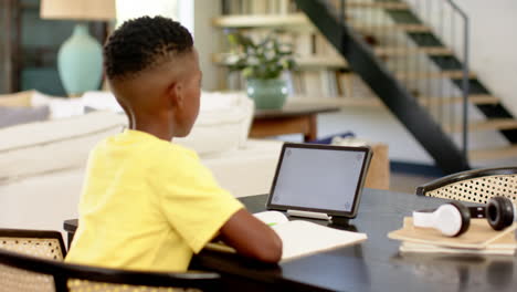 boy studying at home using tablet and notebook, focusing on schoolwork, copy space