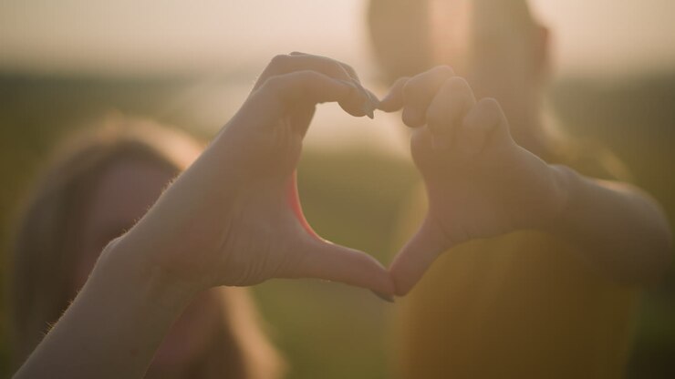 A beautifully blurred shot captures the tender moment of a young boy and a woman forming a heart shape with their hands against the backdrop of a serene sunset
