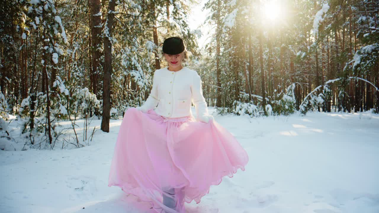 Donna elegante in abito rosa che passeggia in una foresta innevata