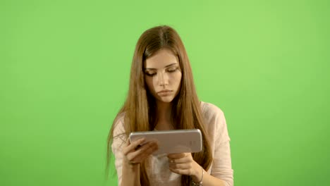 un hermoso modelo se ve y lee en la tableta. en el fondo de una pantalla verde