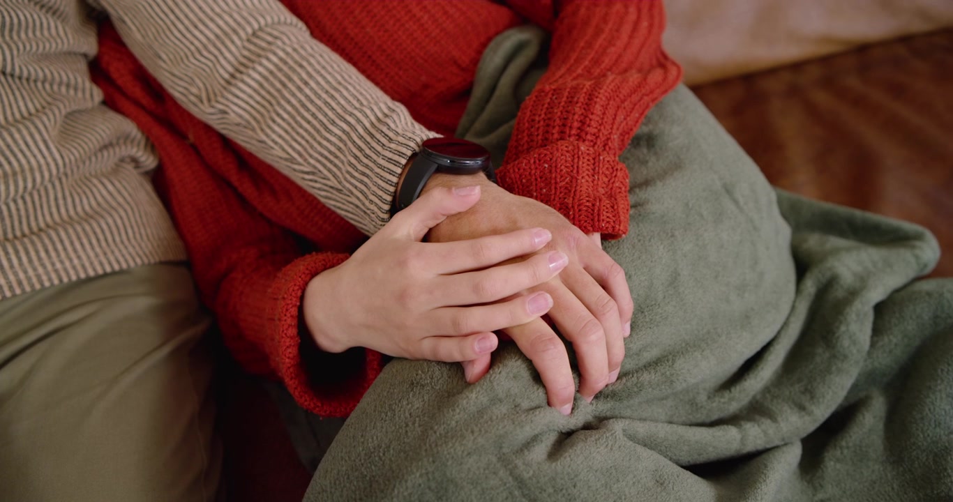 Smaller hand is covering and clasping watch, wrapping and stroking fingers for comfort on blanket