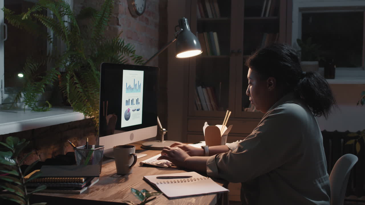 Woman working late at night on a computer in a dimly lit home office