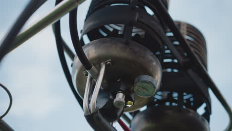 close up of hot air balloon burner shaking on metal frame under cloudy sky as pilot tests equipment safety and gauges during preflight setup against soft background