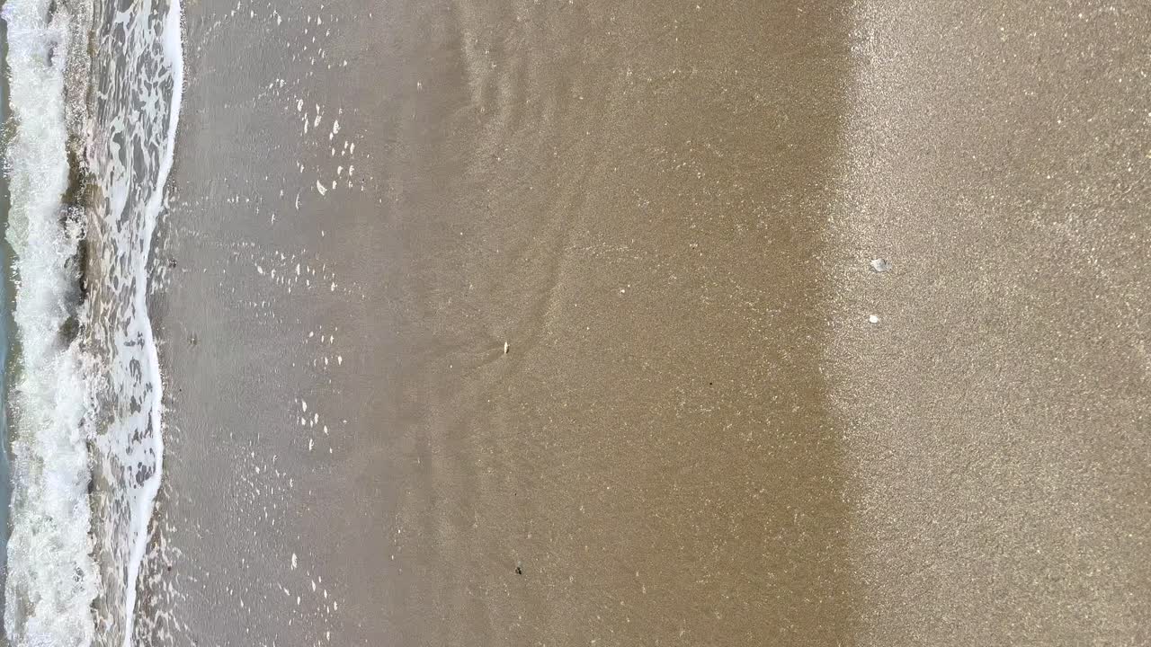 Skum med havets bølger på stranden set fra en vertikal optagelse, vertikal visning.