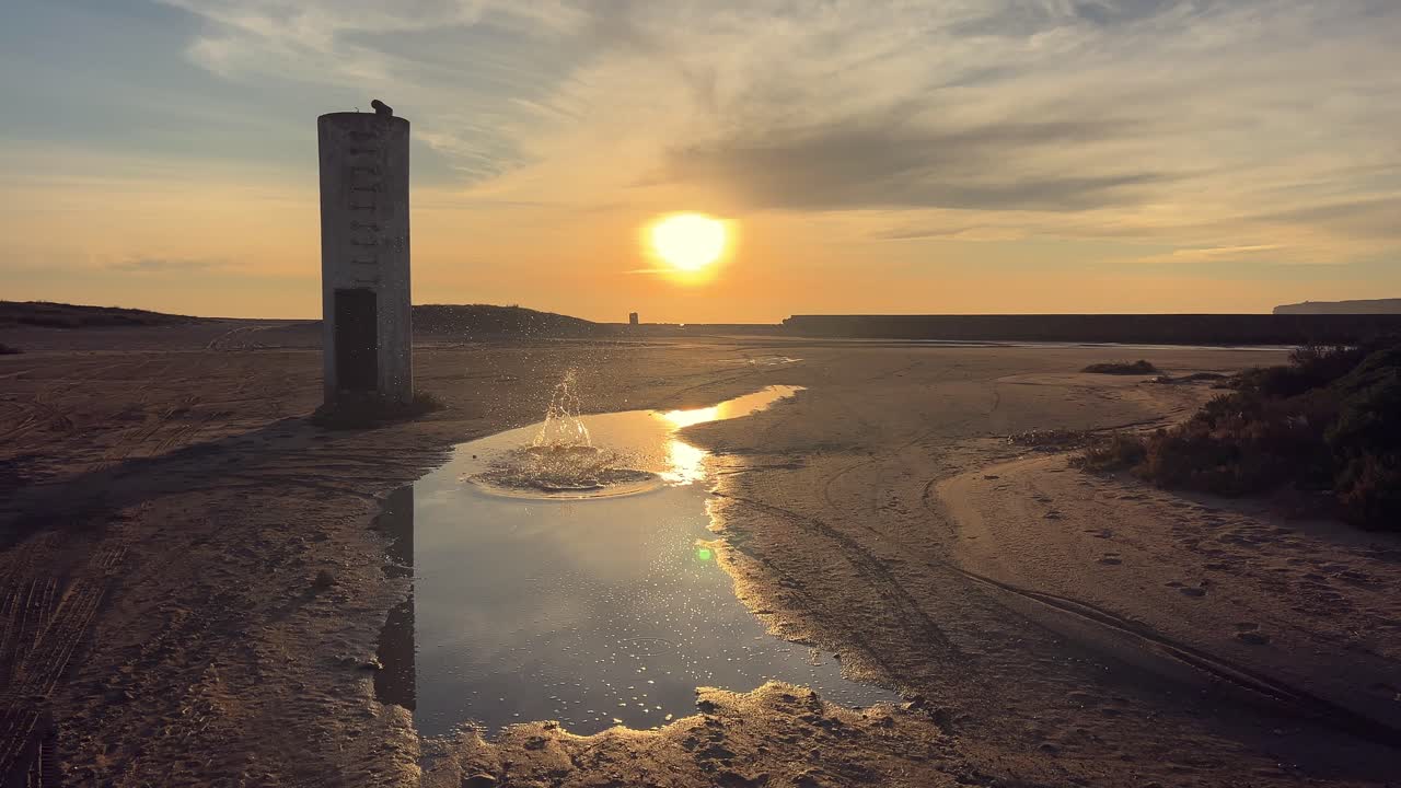 piedra salpicando en un charco de agua rodeado de arena y con el reflejo del sol al atardecer.