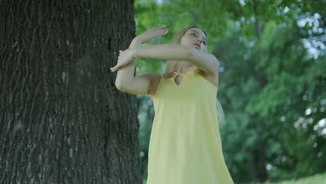 mujer con vestido amarillo bailando junto al árbol en el parque de verano
