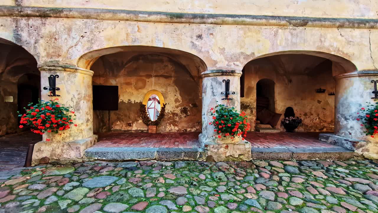 Cobblestone path into the historic courtyard of Jaunpils Castle, revealing the beautiful and rustic arched arcade of the ancient medieval fortress in Latvia - smooth push-in shot