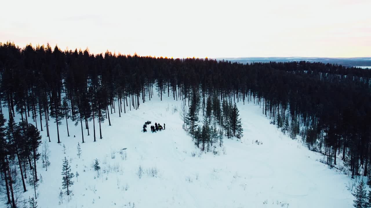 drone shot of a group of people standing on top of a mountain with snowmobiles during sunset from the distance