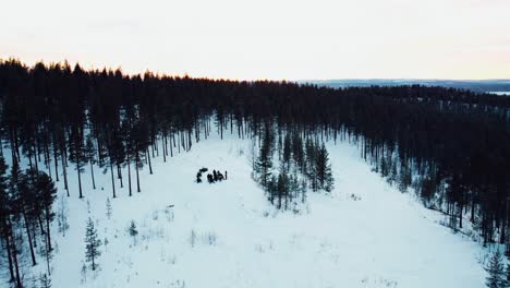 toma de drone de un grupo de personas paradas en la cima de una montaña con motos de nieve durante la puesta de sol desde la distancia
